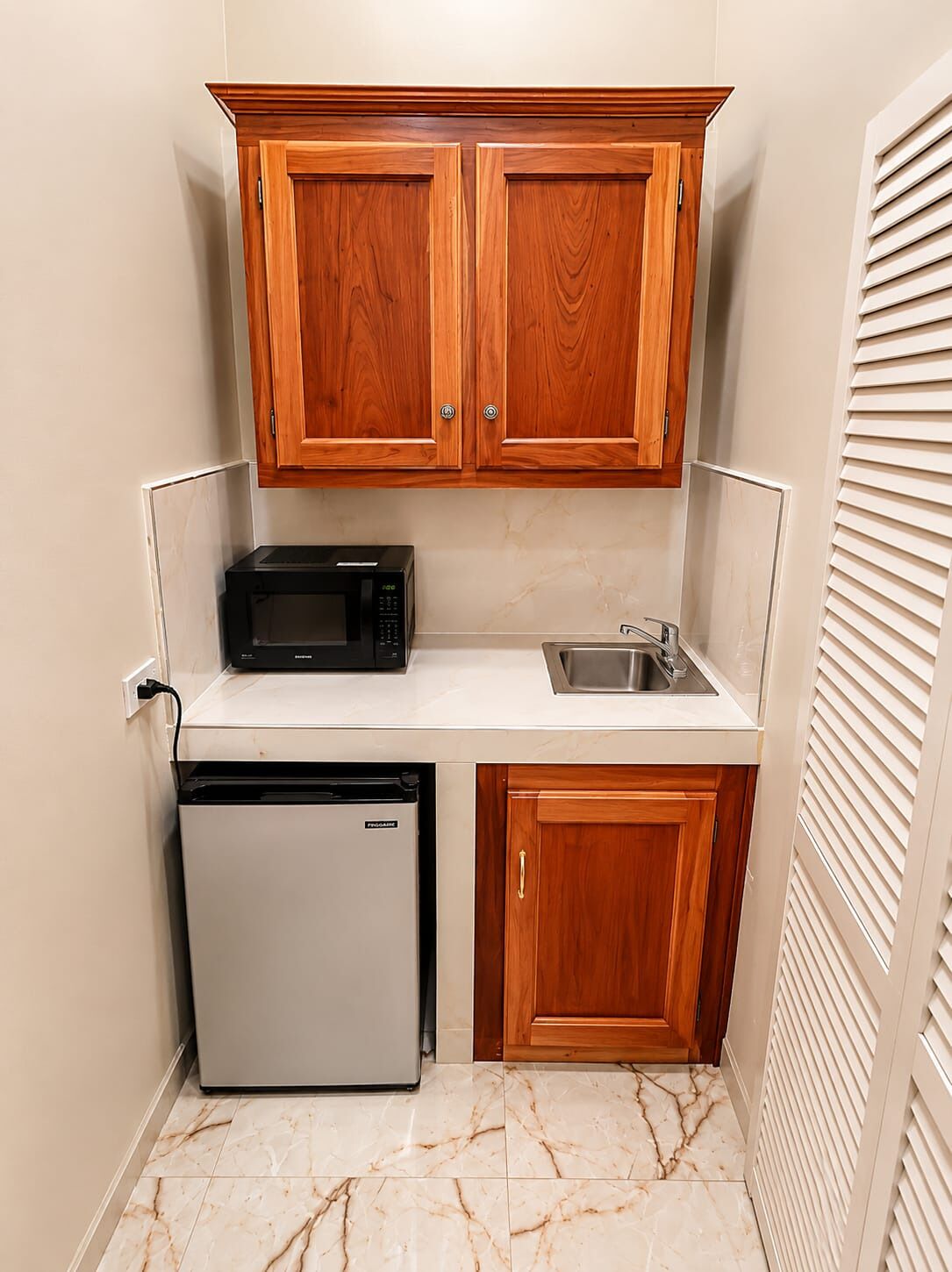 A compact kitchen with wooden cabinets, a microwave, a sink, and a dishwasher.