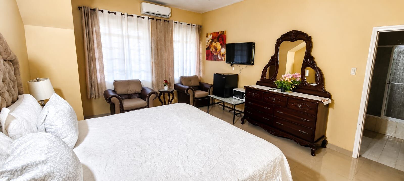 Una habitación de hotel con una cama, dos sillones, un televisor, un aparador y un espejo.