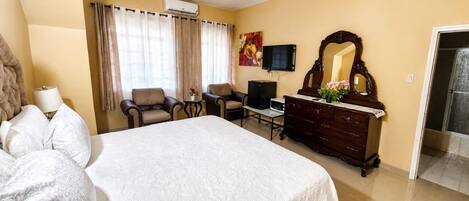 Una habitación de hotel con una cama, dos sillones, un televisor, un aparador y un espejo.