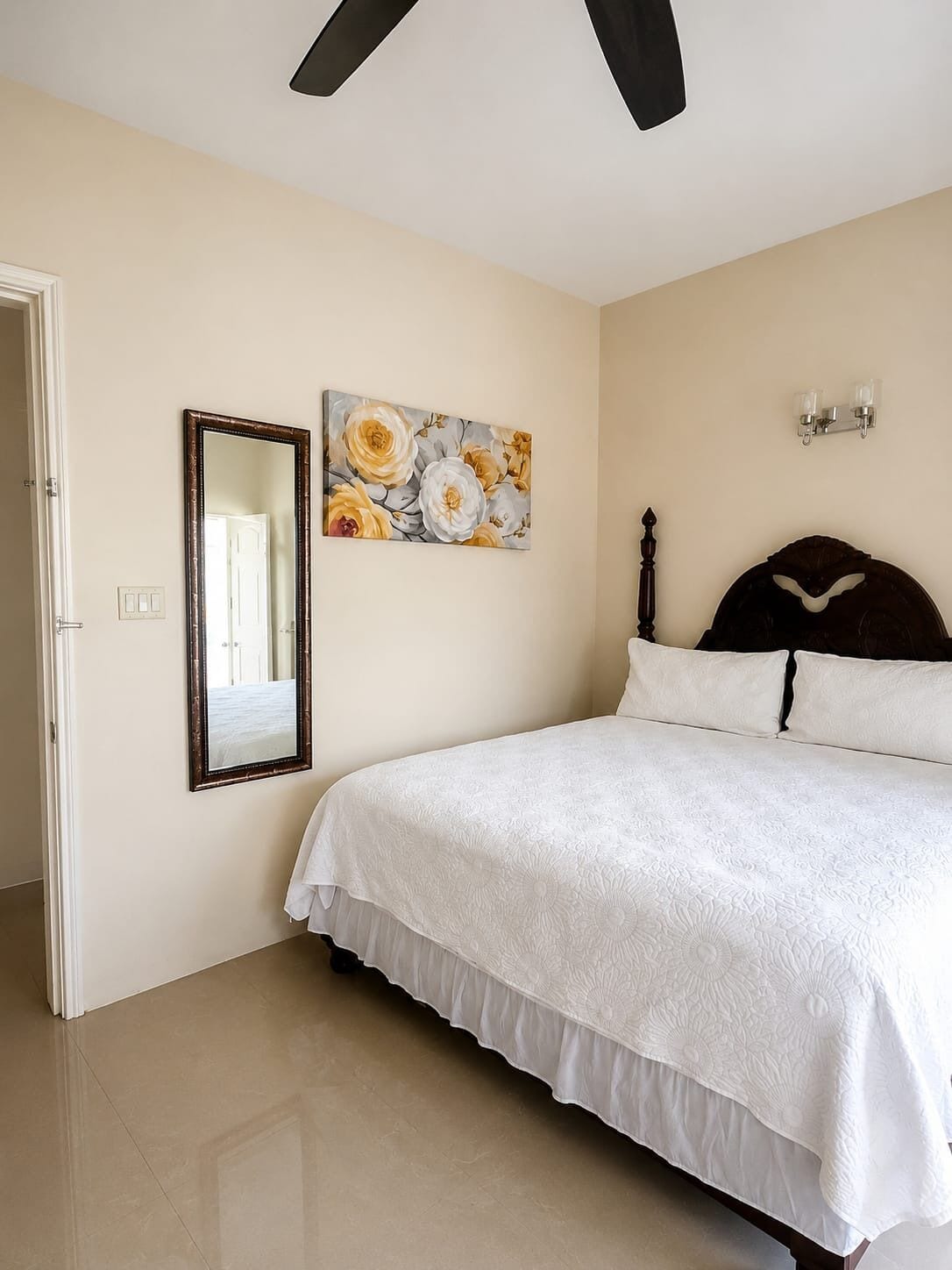 Quarto com cama, espelho, pintura, ventilador de teto e mesa de cabeceira.