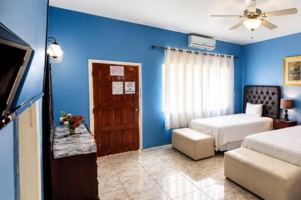 Une chambre avec deux lits, un ventilateur de plafond, une porte avec une pancarte et une fenêtre avec des rideaux.