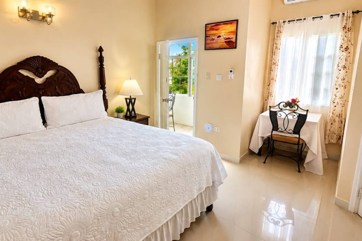 Une chambre avec un grand lit, une table de chevet avec une lampe, une chaise, une porte donnant sur un balcon et un tableau au mur.