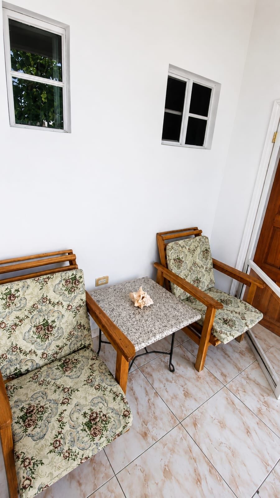 A corner room with two wooden chairs, a small table, and two windows.
