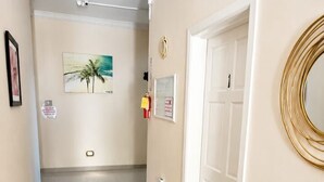 A hallway with a white door, a framed picture, a wall-mounted mirror, and a ceiling light. - Dela de-Rose Guest House negril Jamaica (Negril)