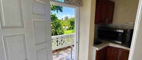 A kitchen with a microwave, wooden cabinets, and a view of a green garden through an open door.