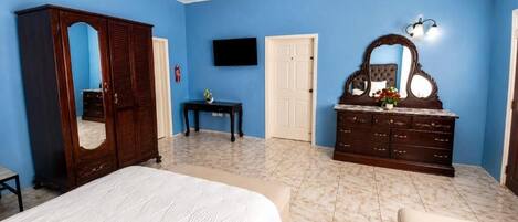 A bedroom with a bed, a wardrobe, a dresser, a television, and a door.