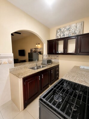 A kitchen with dark wood cabinets, a granite countertop, a stainless steel sink, and a black gas stove. - Dela de-Rose Guest House negril Jamaica (Negril)