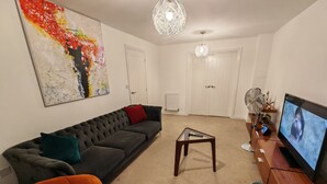 Una sala de estar con un sofá modular, una mesa de centro de vidrio, un televisor y un cuadro en la pared.