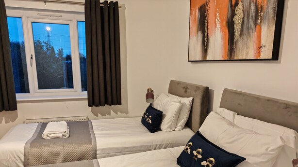 Habitación de hotel con dos camas individuales, un ventanal con cortinas, un cuadro en la pared y vistas a árboles desde el exterior.