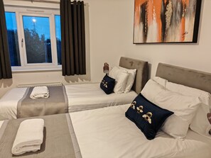 Une chambre d’hôtel avec deux lits simples, une grande fenêtre avec des rideaux, un tableau au mur et une vue sur les arbres à l’extérieur.