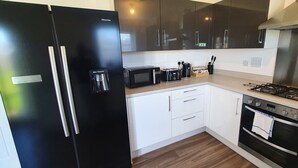 Una cocina moderna con un refrigerador negro, un microondas, una estufa a gas y muebles de cocina blancos.