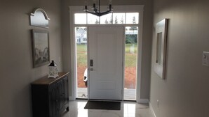 Uma entrada limpa e moderna, com uma porta branca, um console de madeira escura e um candelabro.