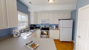 A compact kitchen with white cabinets, a microwave, stove, and refrigerator. - Entire Townhouse in Rock Hall (Rock Hall)