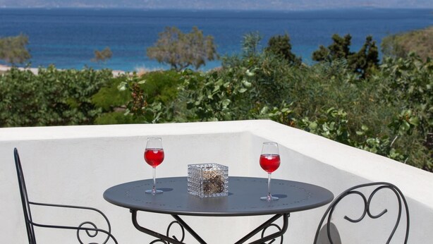 Une table avec deux verres de vin rouge et un vase décoratif, le tout placé devant un paysage pittoresque de mer et de montagnes.