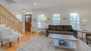 A spacious living room with hardwood floors, a brown leather sofa, a gray armchair, a coffee table, and a ceiling fan. - Southern City Comfort - Huge Private Backyard (Nashville)