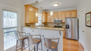 A kitchen with wooden cabinets, a stainless steel refrigerator, a microwave, and a bar area with chairs. - Southern City Comfort - Huge Private Backyard (Nashville)