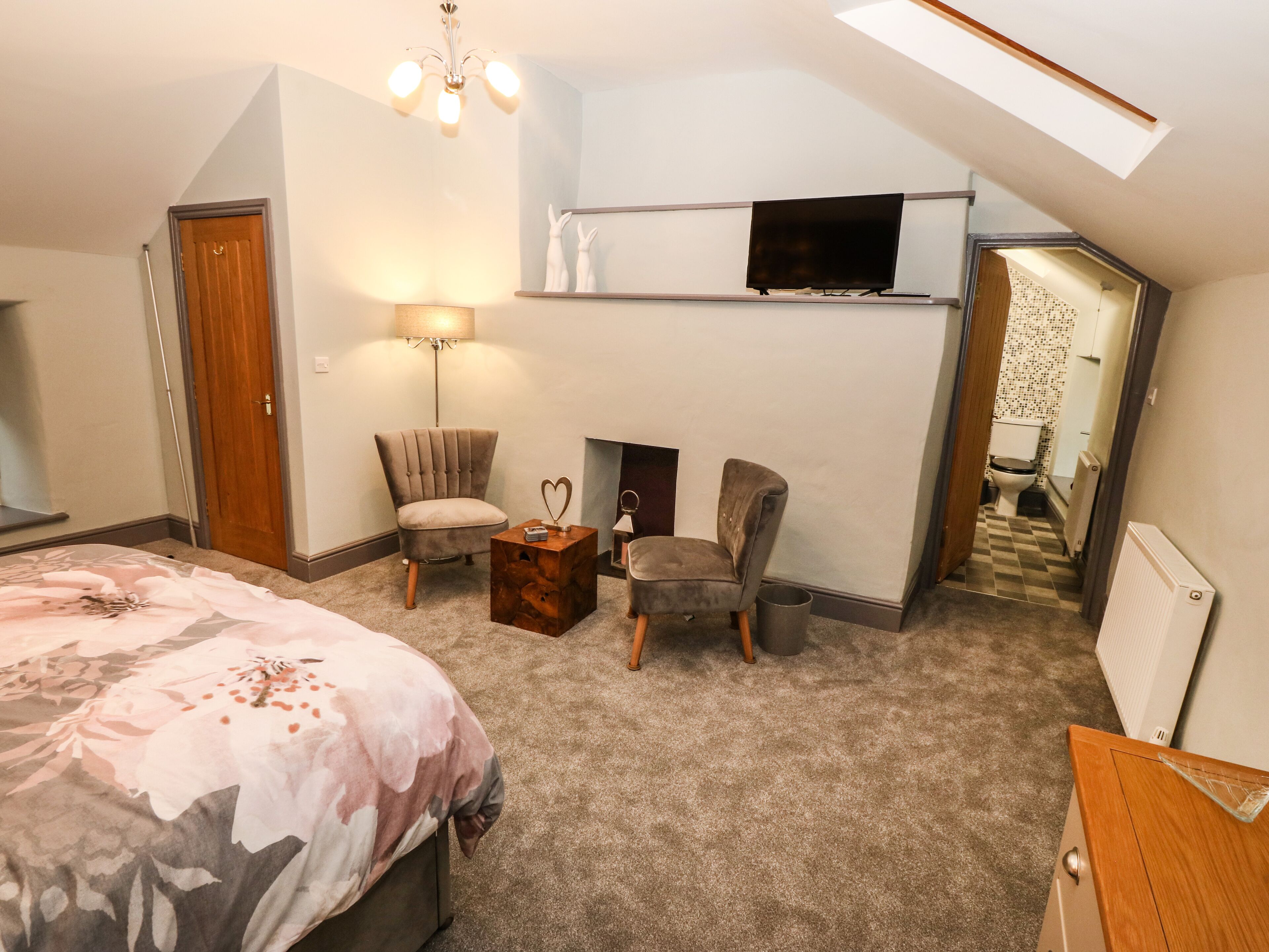 A bedroom with a bed, two chairs, a TV, a lamp, and a fireplace.