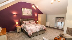 A bedroom with a bed, bedside tables, a wardrobe, a window with a view, and a chair. - Bryn Aber Bach (Pwllheli)