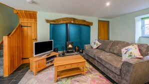 A living room with a wooden staircase, a TV, a fireplace, and a couch. - Bryn Aber Bach (Pwllheli)