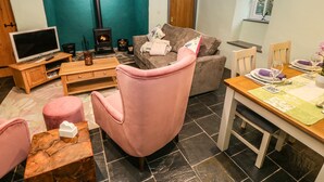 A cozy living room with a television, a fireplace, a sofa, and a dining area with a table set for two. - Bryn Aber Bach (Pwllheli)
