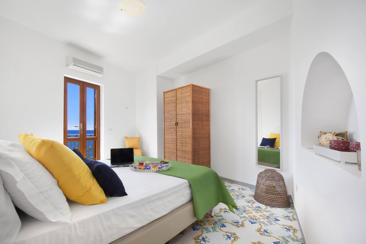 A bedroom with a bed, a wardrobe, a mirror, and a window with a view.