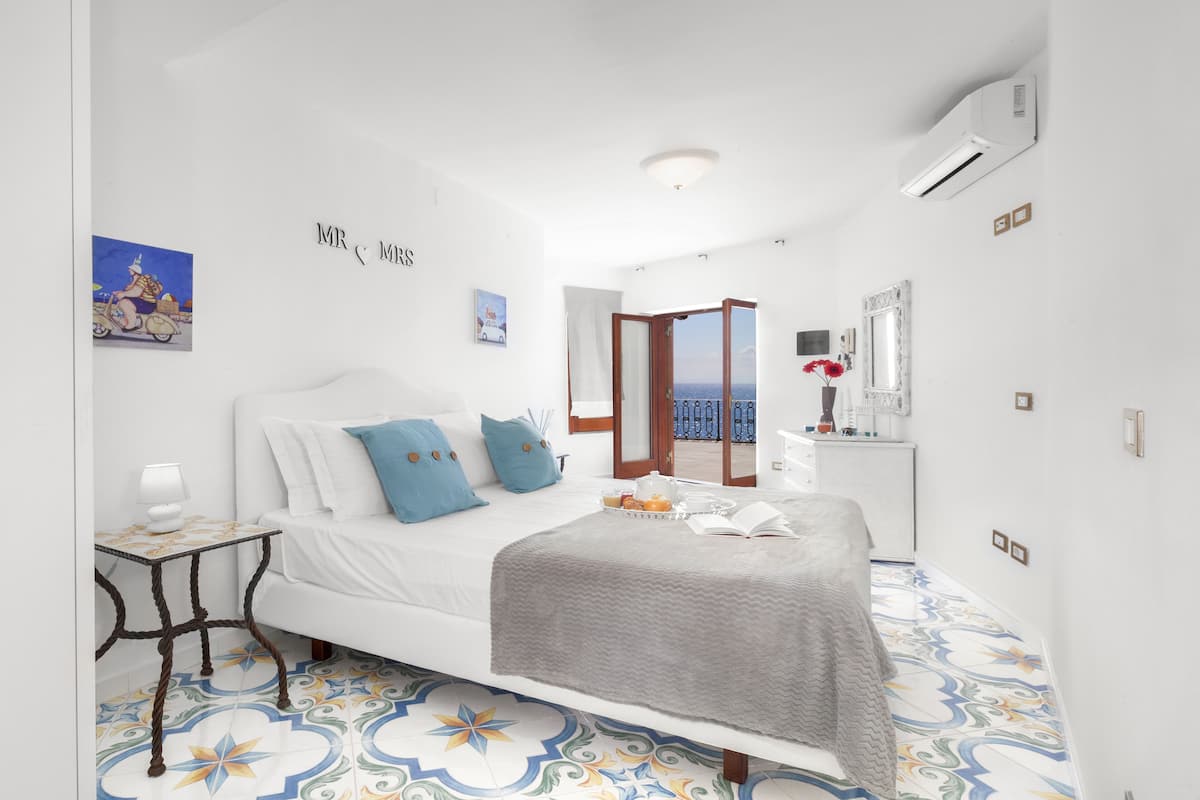 A bedroom with a bed, bedside table, and a view of the sea through an open door.