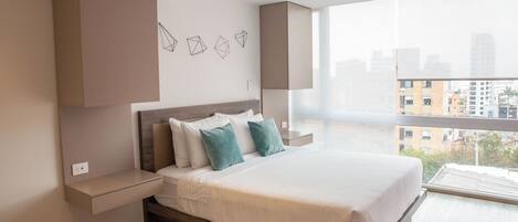 Habitación de hotel moderna con una cama grande, mesitas de noche empotradas, vistas a la ciudad y un cuadro de arte mural geométrico.