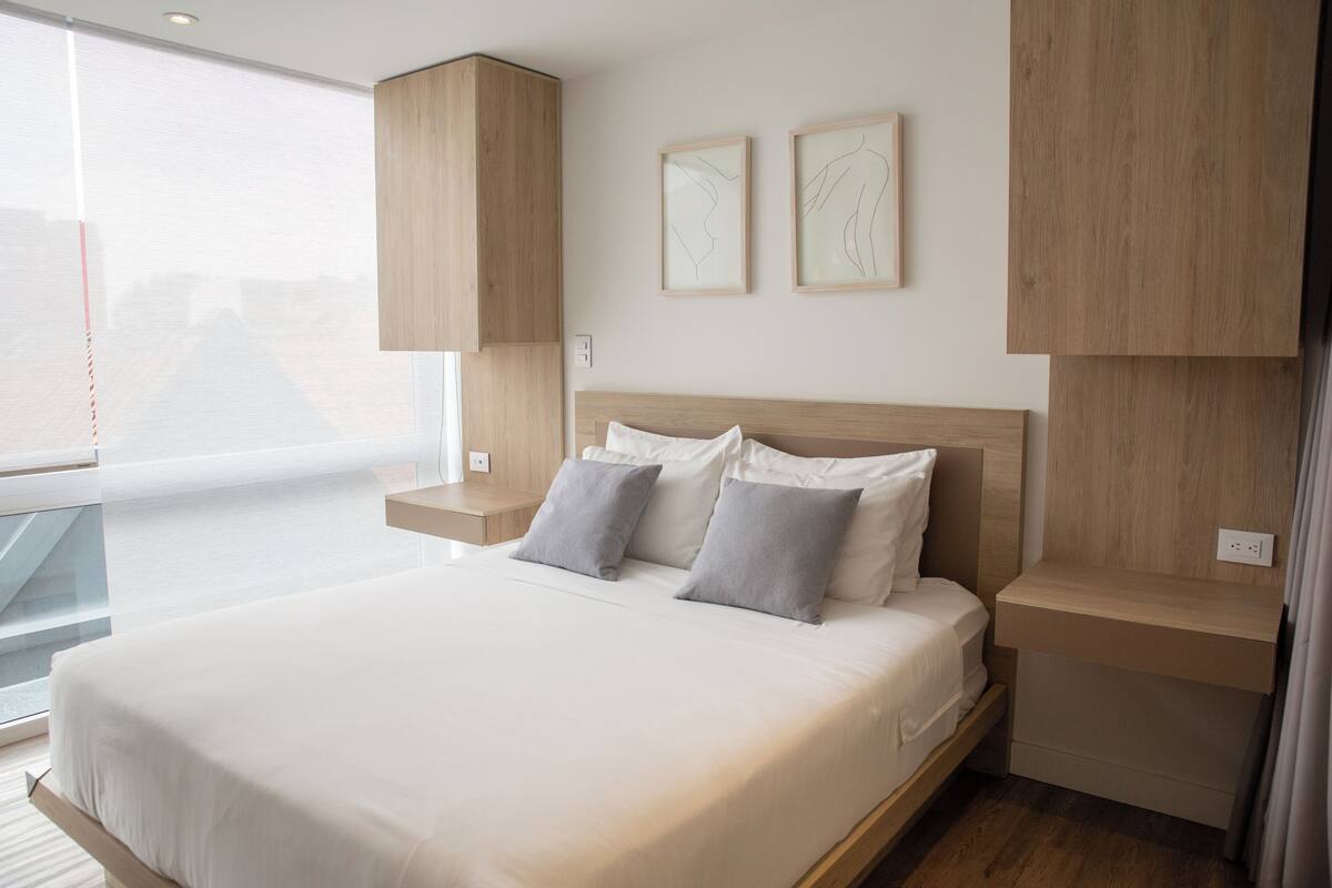 Ein modernes Schlafzimmer mit einem großen Bett, einem Holzkopfende, Nachttischen und Bildern an der Wand.