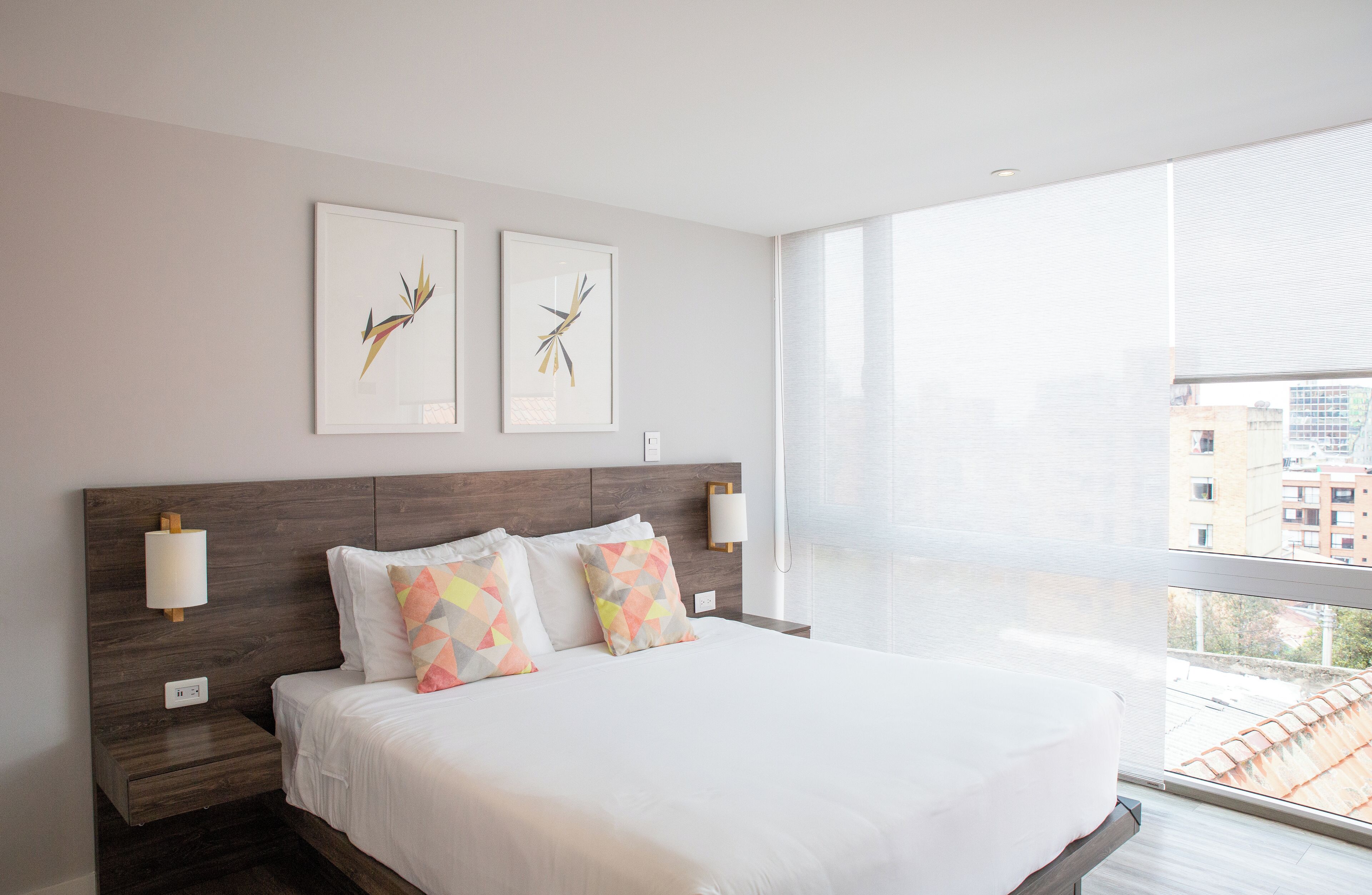 A modern hotel room with a large bed, two wall-mounted lamps, and two framed abstract artworks.