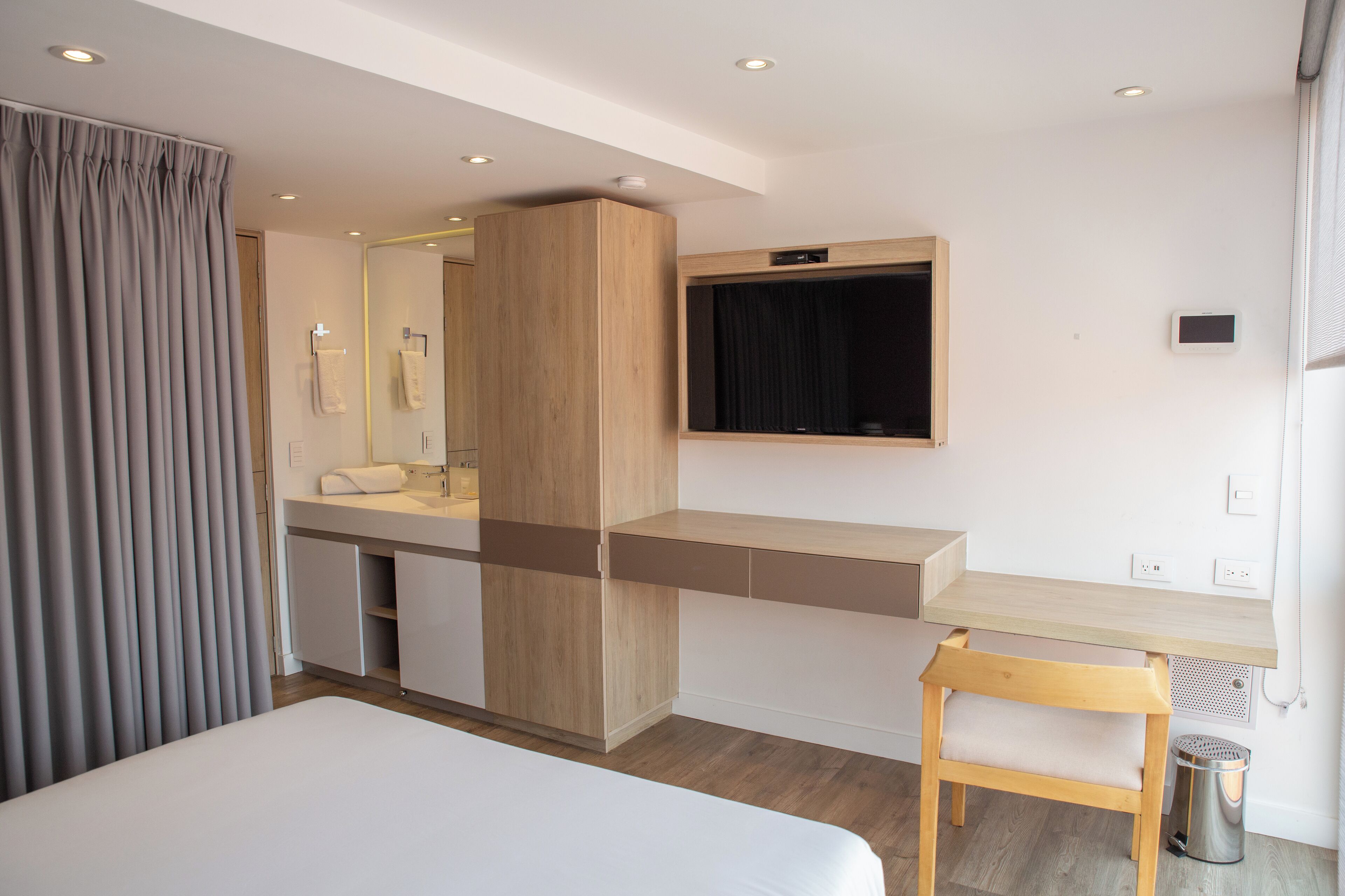 Una habitación de hotel moderna con una cama grande, un escritorio de madera, una tocador empotrado y un espejo amplio.
