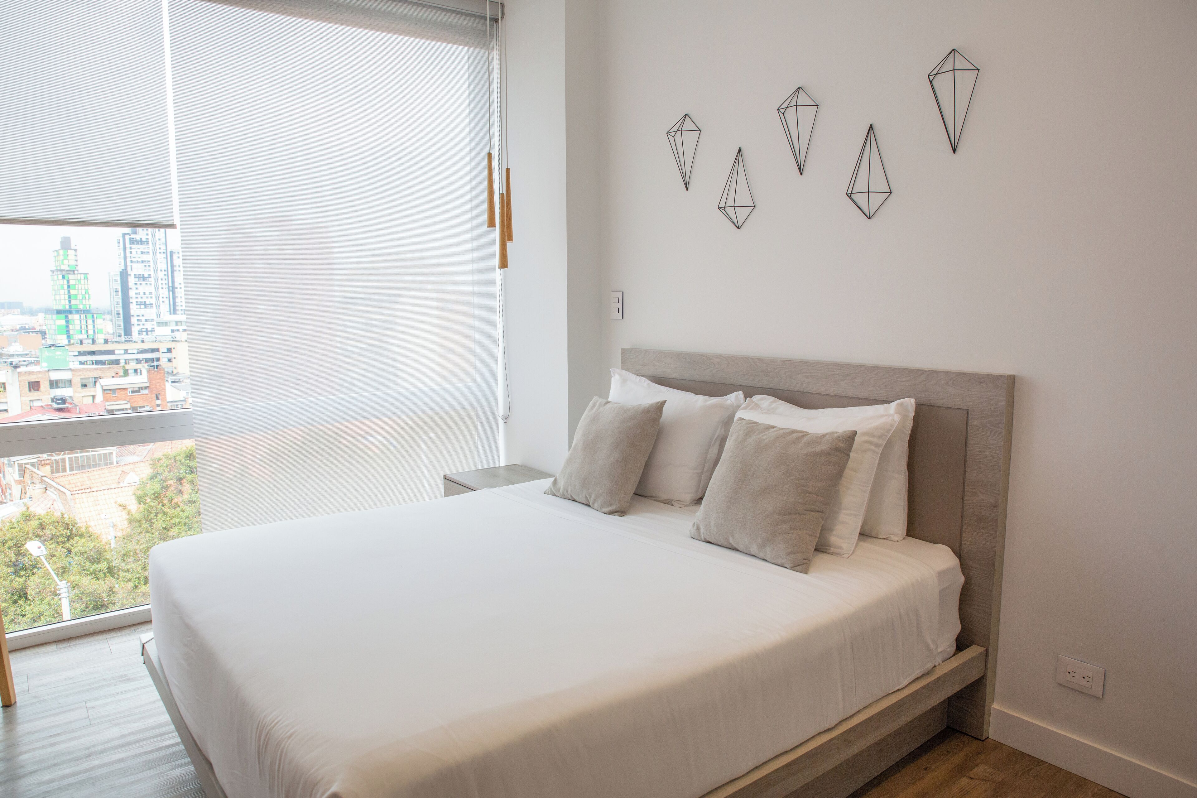 A modern bedroom with a large bed, a city view, and geometric wall art.