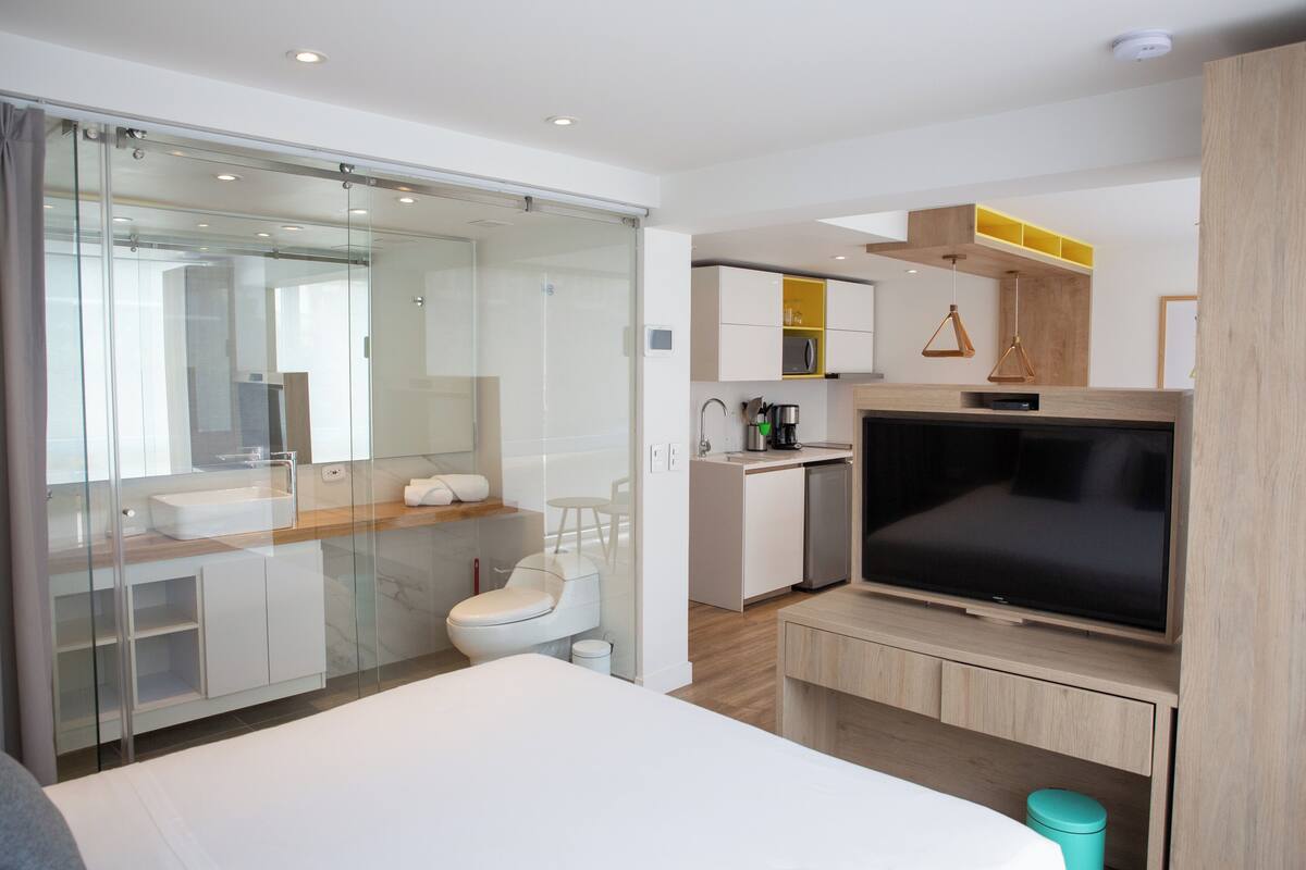 Ein modernes Hotelzimmer mit Duschkabine, Bett, Fernseher, Küchenzeile und Badezimmer.