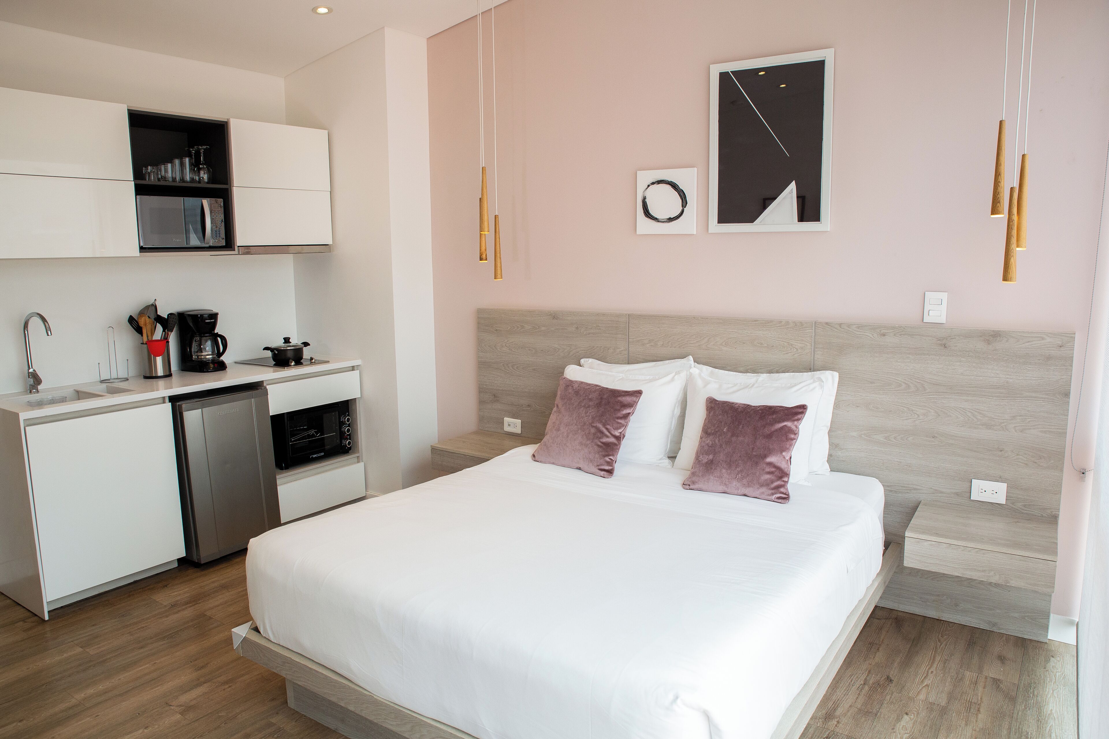 A modern hotel room with a bed, bedside table, and a kitchenette with a coffee maker and microwave.