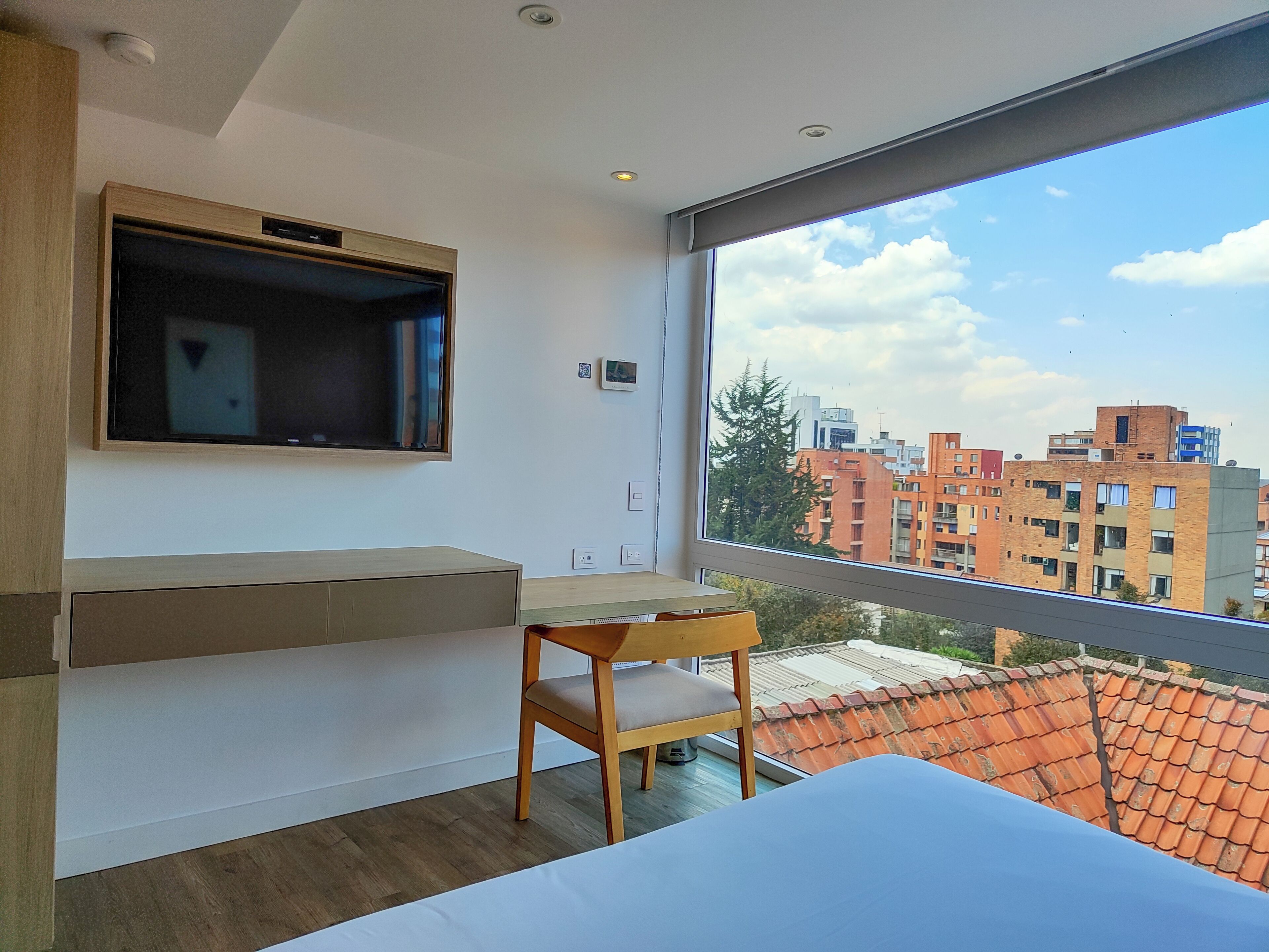 Ein modernes Schlafzimmer mit großem Fenster, einem Flachbildfernseher, einem Holztisch und einem Bett.