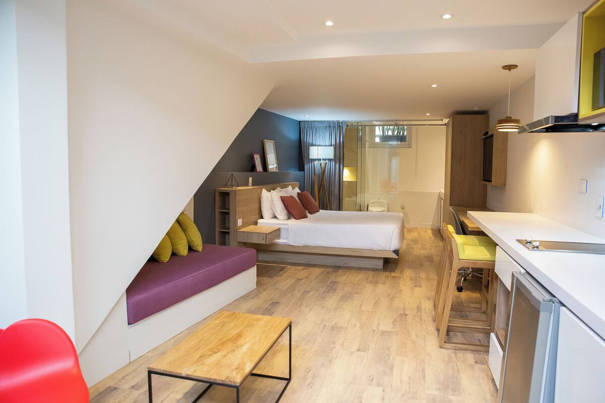 Ein modernes Hotelzimmer mit Schlafgalerie, einer kleinen Sitzecke, einer Küchenzeile und einem Badezimmer mit Glasdusche.