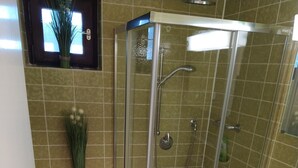 Un baño con ducha envuelta en vidrio, un inodoro con cubierta decorativa y un lavamanos con una botella de champú.
