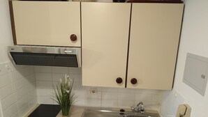 Cocina compacta con cocina por inducción negra, pileta de acero inoxidable y muebles color beige con pomos redondos.