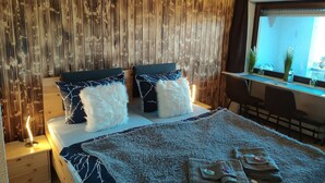 Un dormitorio con pared de paneles de madera, cama con ropa de cama blanca y azul, un escritorio con computadora y una ventana con vistas.