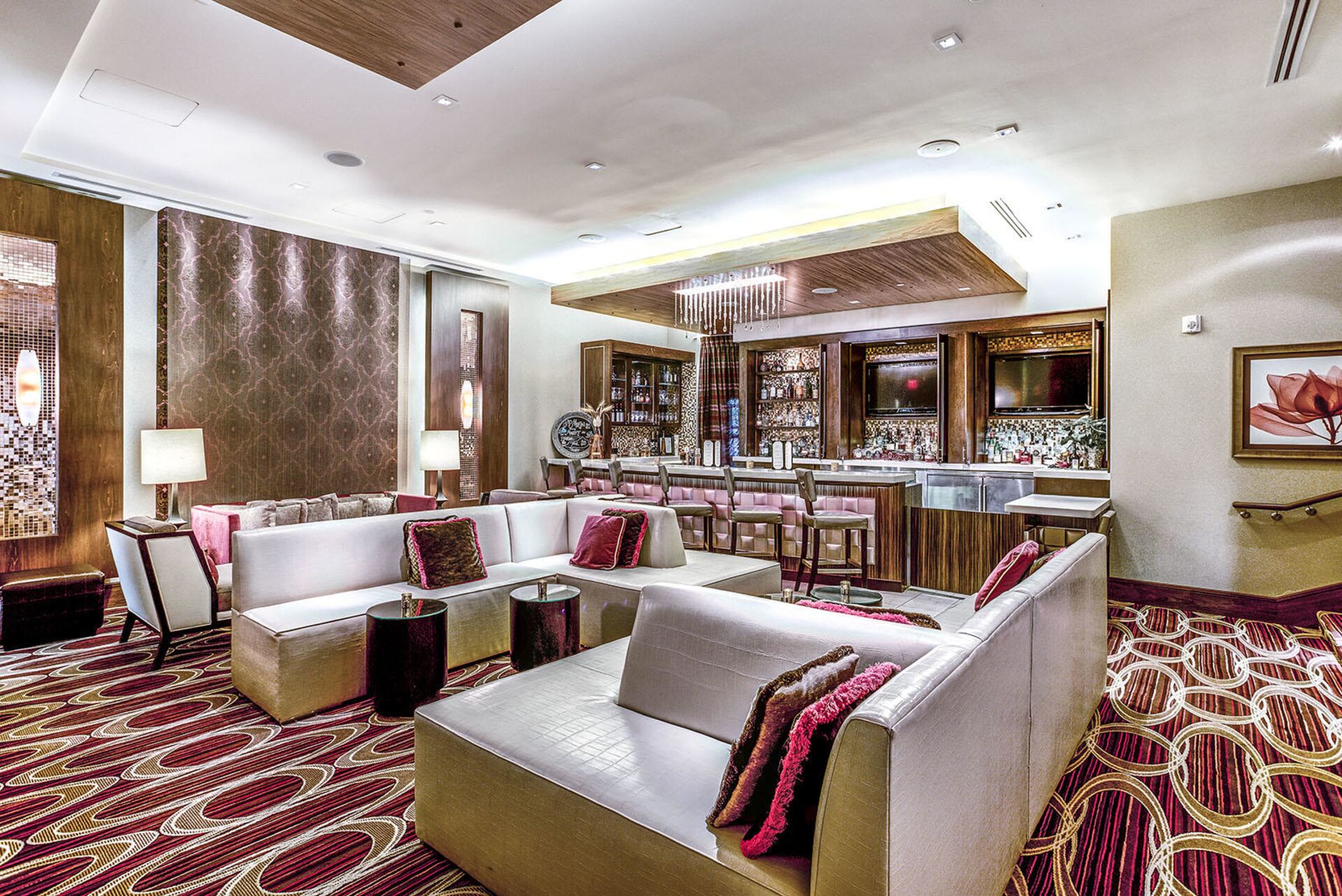 A modern hotel lobby with a bar area, seating arrangements, and a patterned carpet.