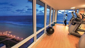 A gym with a large window overlooking a beach at dusk. - Two Bedroom Luxury Suite, Ocean View, Virginia Beach, Virginia (2555337) (Virginia Beach)