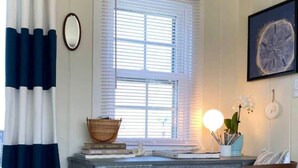 Ein Arbeitszimmer mit Schreibtisch, Stuhl und einem Fenster mit Jalousien.
