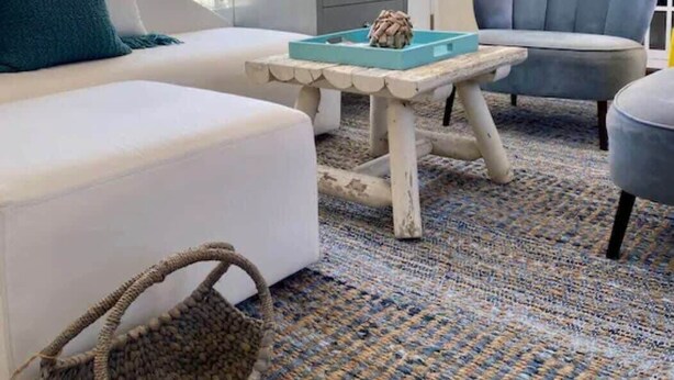 Ein modernes Wohnzimmer mit einem weißen Sofa, einem grauen Sessel, einem blau-weißen Streifen Teppich und einem kleinen Tisch mit einer Dekoration.