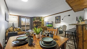 Un coin repas avec une table en bois dressée pour quatre personnes, un mur décoratif en pierre et un espace salon confortable avec un canapé et des fauteuils.