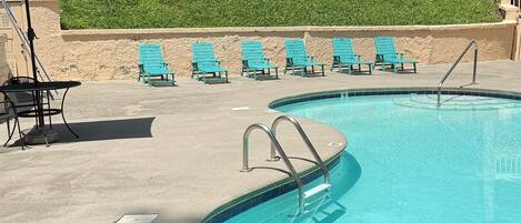Una piscina con una pared de piedra, una escalera metálica y varias sillas de descanso azules.