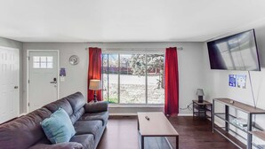 Un salon avec un canapé, une table basse, un téléviseur et une fenêtre avec des rideaux.