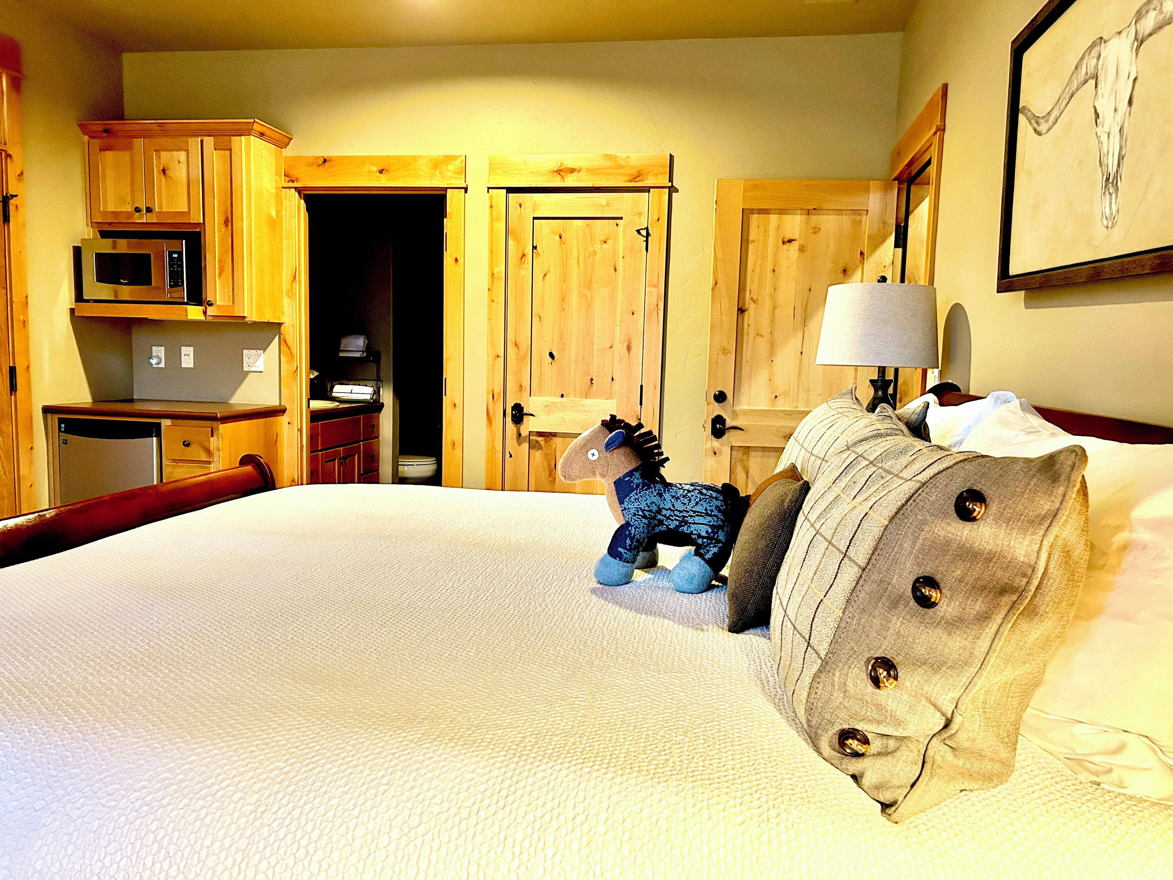 A hotel room with a bed, a wooden wardrobe, a microwave, and a door leading to a bathroom.