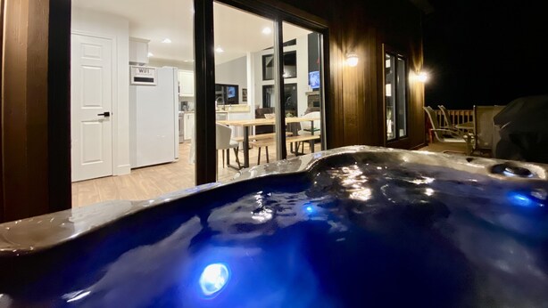 A hot tub with a wooden deck and a view of a house interior with a kitchen and dining area. - Hot Tub & Sauna ~ The Ridge Chalet ~ Wood Fireplace ~ Sleeps 12 (Great Valley)