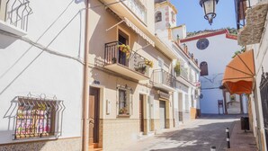 Une rue étroite bordée d’immeubles dotés de balcons et surmontée d’un clocher.