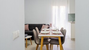 Un espace repas moderne avec une table dressée pour quatre personnes, un canapé et un coin cuisine visible au fond.