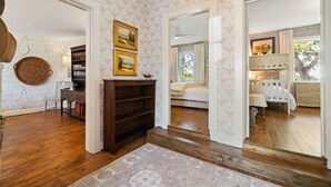 Ein Zimmer mit Holzboden, einem gemusterten Teppich, einem Bücherregal und einem Bett mit Blick ins Freie.